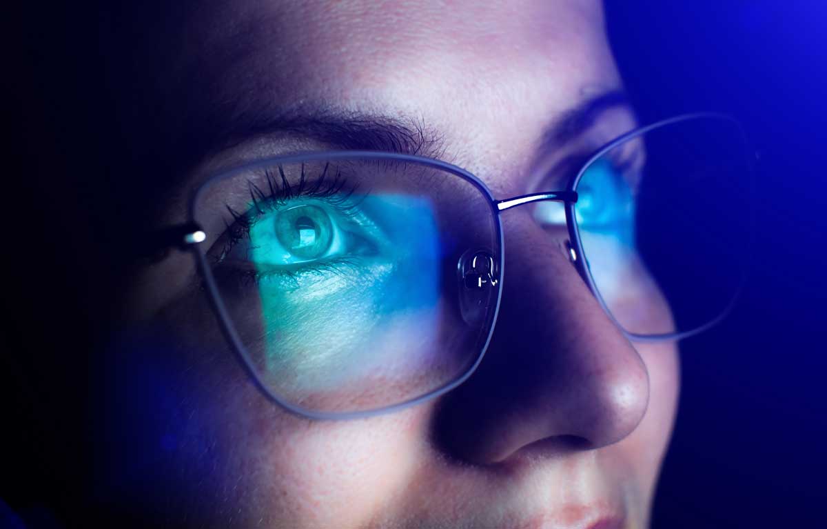 czytanie e-booka w okularach filtrujących światło kobieta czyta e-book w fotelu nosząc okulary z filtrem niebieskim wieczorem